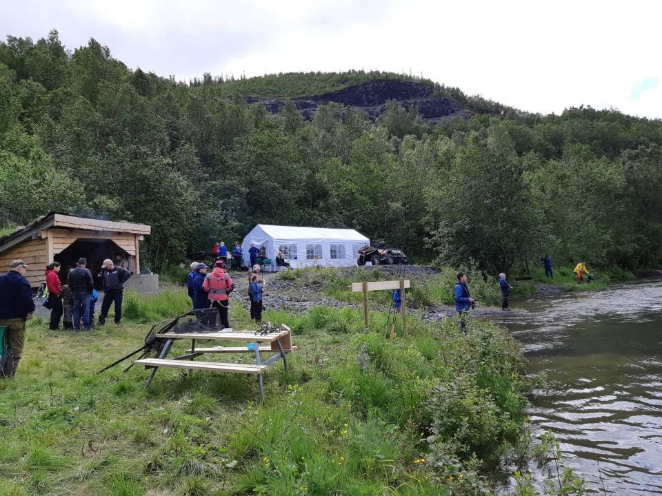 Oversiktsbilde som viser aktiviteten i sentralområdet med aktive fiskere, deres hjelpere, gapahuk, ildsted, grill og arrangørtelt.