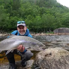 Person med laks i henderne fremfor elva