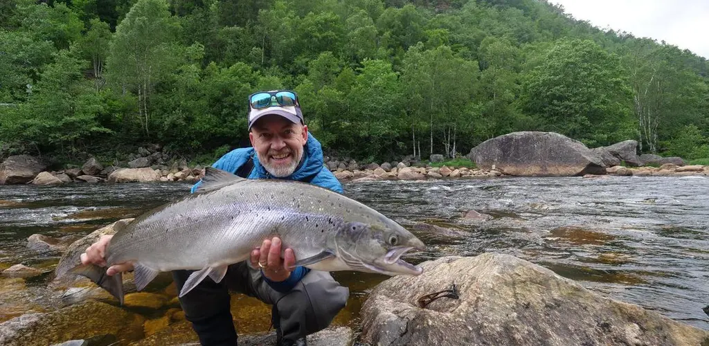 Person med laks i henderne fremfor elva