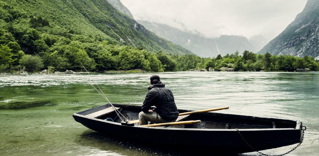 Laksefisker i båt ved elvebredden.
